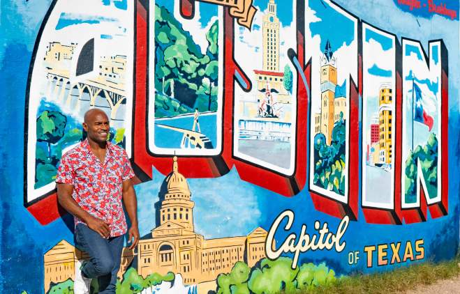 Man in patterned shirt leaning against the "Greetings from Austin" postcard mural.