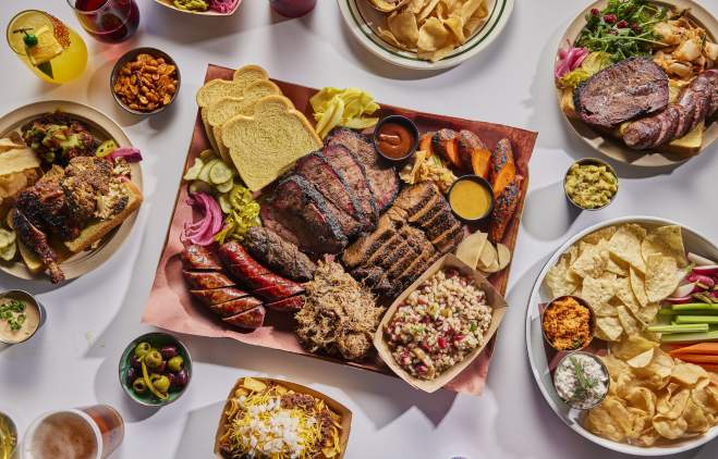 Colorful plates and trays of LeRoy and Lewis Barbecue, including sausage, brisket, frito chili pie, chips and crudite and more.