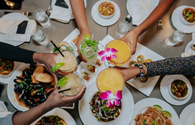 Five hands holding cocktails and reaching in to cheers at Mandala Kitchen and Bar