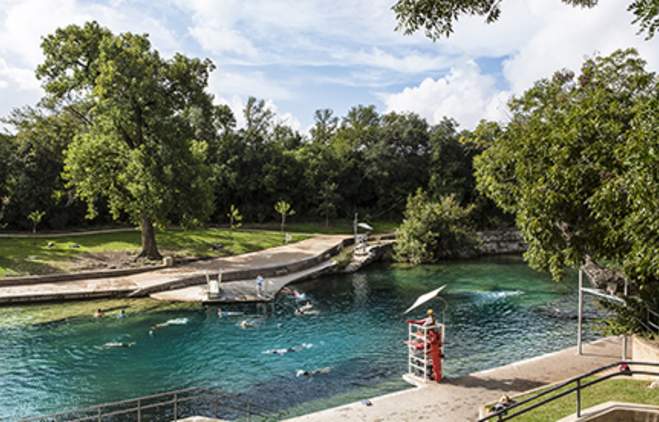 People swimming in Barton Springs Pool with lifeguard in stand