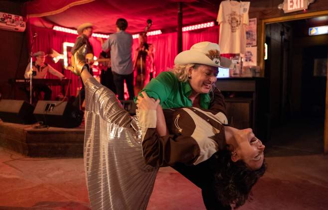 Two women in Western attire country dancing in a dance hall.