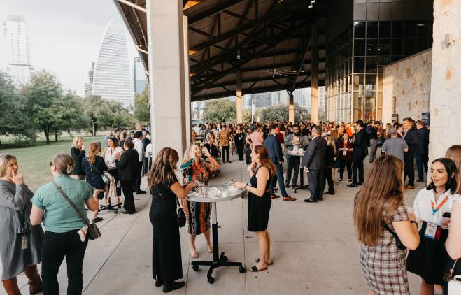 People with event badges on standing under the pavilion at Palmer Events Center during golden hour.