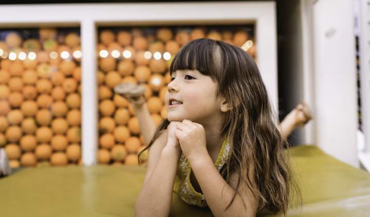 Anaheim Packing House Atrium featuring a child relaxing on a green cushioned seating area, with a decorative wall of oranges in the background inside the historic Anaheim Packing House food hall.