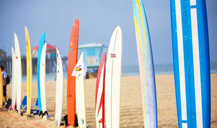 Colorful surfboards lined up on the sand at Huntington Beach, with a lifeguard tower and the ocean visible in the background under a clear blue sky.