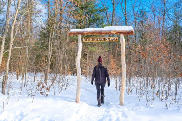person in dark clothes hiking snow covered trails in winter, blue sky