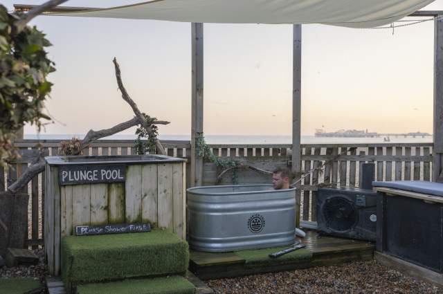 A man sits in a tin ice bath, next to a plunge pool at the Beach Box Sauna, Sussex