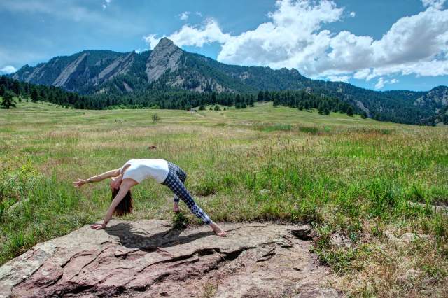 A woman bends into Camatkarasana, also known as Wild Thing pose, near Boulder's Flat Irons.