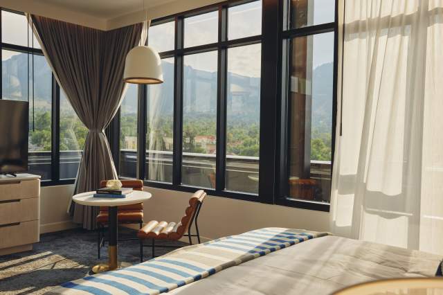 A guest room with television, table and chairs, bed and big windows overlooking the Flatirons in Limelight Hotel, Boulder.