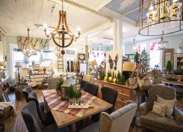 The cozy interior of Old Lucketts Antique Store featuring rustic furniture, decorative items, and warm lighting. A large wooden table is set with greenery.