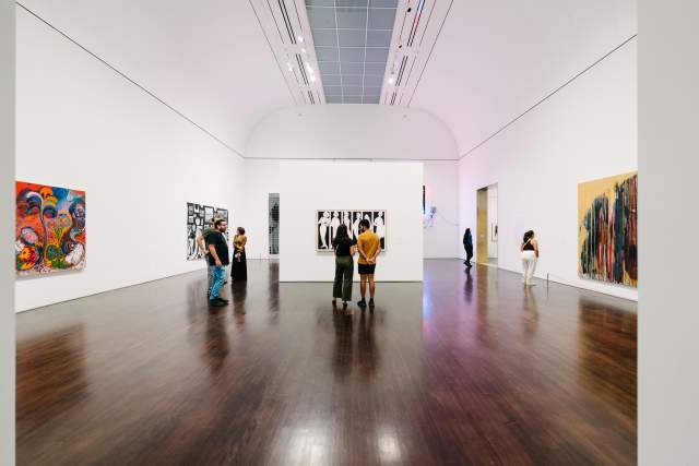 People admiring an art exhibit in a large white room at the Blanton Museum of Art.