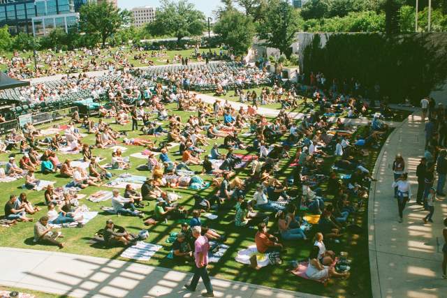 A large group of people sitting on a green lawn in front of a stage for the Austin Blues Festival.