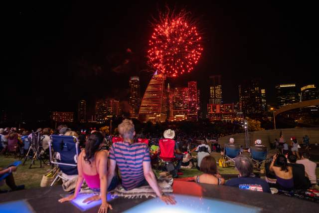 People sitting on the lawn at The Long Center watching fireworks display over the Austin skyline at Star Spangled Fest.