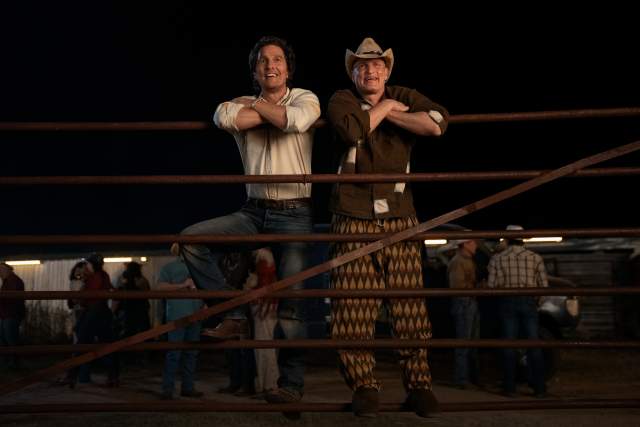Matthew McConaughey and Woody Harrelson leaning on a livestock gate at a rodeo.