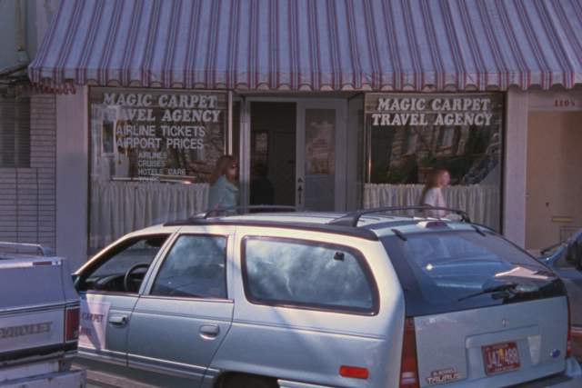 Waiting for Guffman screengrab showing cars parked in front of an office with signs reading Magic Carpet Travel Agency
