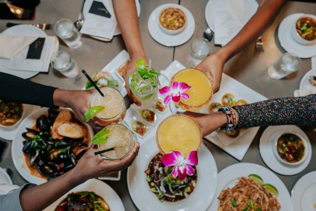 Five hands holding cocktails and reaching in to cheers at Mandala Kitchen and Bar