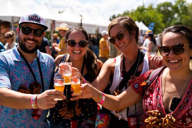 Image of four people at the Texas Craft Brewers Festival hoisting up glasses of beer in a toast while smiling at the camera.