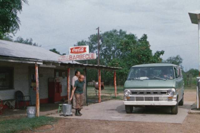 Texas Chainsaw Massacre screengrab, showing a green van parked in front of a gas station with a coca cola and Barbecue sign. Two men walk towards the van