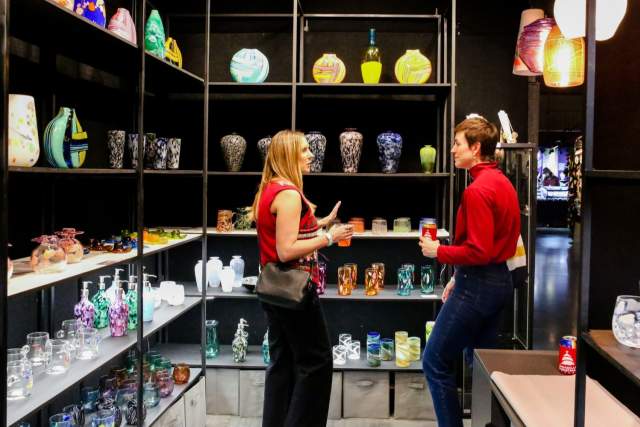 Two women in their early 30s talking in a pop-up shopping display of blown glass works.