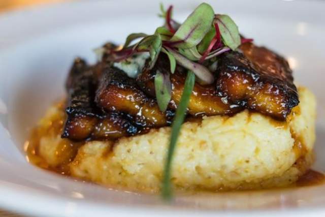 A snapshot of a delicious meal from Pork Belly Oak House. A flavorful meal of mashed potatoes, pork, and greens on top of a white plate.