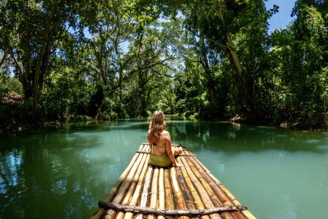 A woman in a green swinsuit sits on a bamboo raft on the Martha Brae River in Montego Bay Jamaica