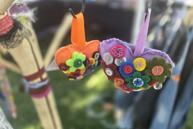 Colorful handmade felt ornaments decorated with flowers and buttons, displayed outdoors at a craft market.