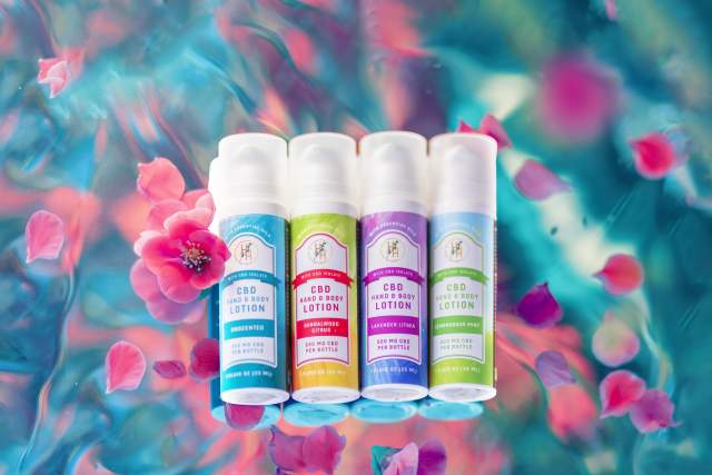 four colorful tubes of CBD hand lotion overlaid on a flowery multicolored background