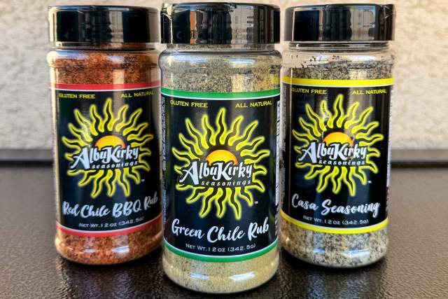 Three seasoning bottles from AlbuKirky Seasonings are displayed against a neutral background. The bottles are labeled "Red Chile BBQ Rub," "Green Chile Rub," and "Casa Seasoning," each with a distinctive yellow sunburst logo.