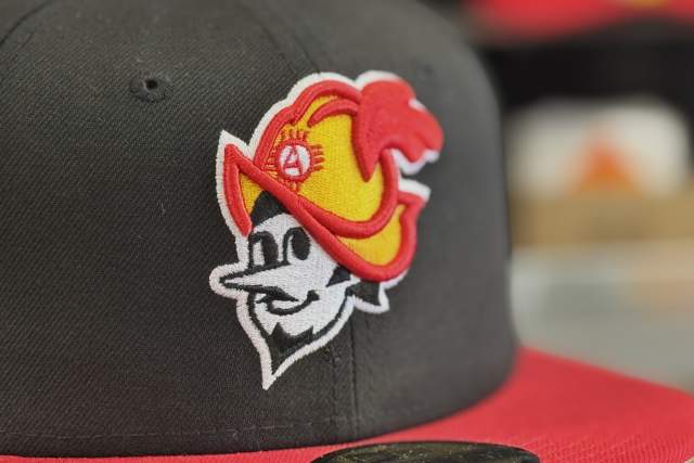 Closeup of a red and black flat brim hat with a character wearing a medieval helmet on it.