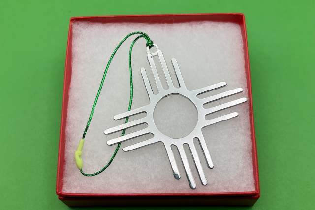 A Zia sun symbol pendant displayed on a green background inside a red box with a white interior.