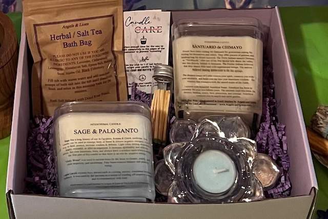 Gift box containing various self-care products including herbal bath tea, sage and palo santo candle, and other items, arranged neatly in a purple box.
