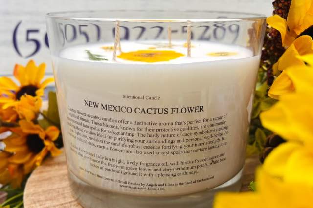 A candle labeled "New Mexico Cactus Flower" by Angels and Lions surrounded by yellow flowers on a wooden surface.