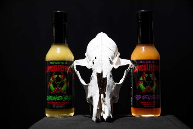 Two bottles of hot sauce labeled "PickleVyper" and "3rd Degree" flanking an animal skull on a dark background.
