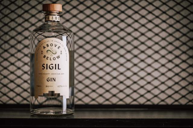 A bottle of Above & Below Sigil Dry Gin displayed in front of a patterned backdrop.