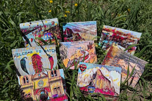 A collection of colorful postcards featuring various famous locations, displayed on a grassy field with wildflowers.