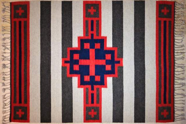 This image shows a traditional Navajo rug featuring bold vertical stripes with intricate geometric patterns in the center and corners. The rug has fringed edges.