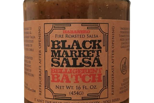 A jar of Black Market Belligerent Batch fire roasted salsa, labeled clearly with the product name and net weight of 16 fl oz. The label features a quote, "It ain't the heat, it's the humility" by Yogi Berra.