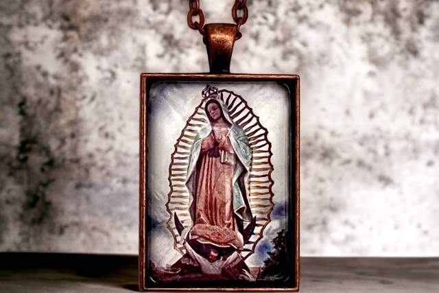Close-up of a pendant featuring an image of Our Lady of Guadalupe, hanging on a copper chain with a textured background.