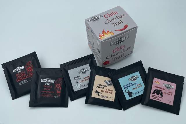 An assortment of Endangered Species Chocolate bars in various flavors, including dark, milk, and filled chocolates, displayed around an open box labeled "Chile Chocolate Trail".
