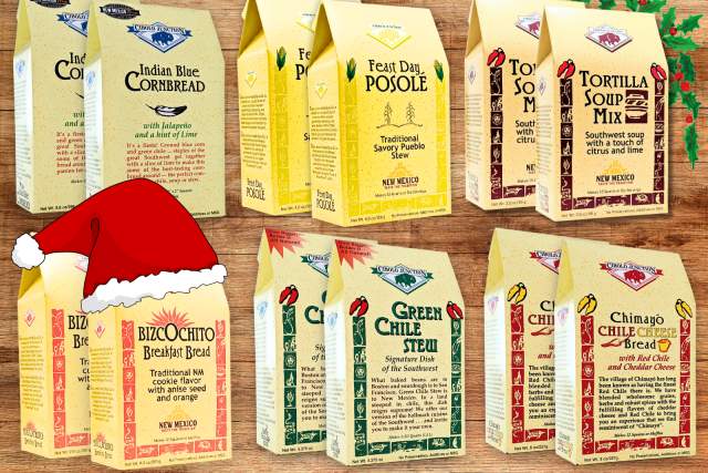 Assorted packages of New Mexico-themed food products, including Indian Blue Cornbread, Feast Day Posole, Tortilla Soup Mix, Biscochito Breakfast Bread, Green Chile Stew, and Chile Chimayo Bread Mix, displayed with a festive Santa hat and holiday decorations.