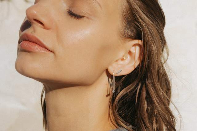 A person lit by bright sun wearing an earring resembling a bike-lock in front of a blank background.