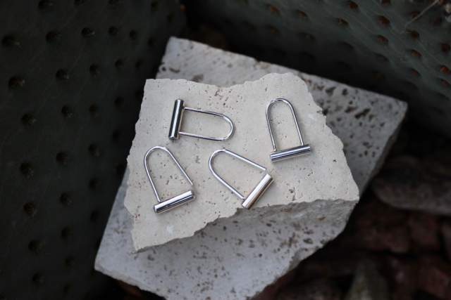 Silver earrings resembling bike locks displayed on broken stone.