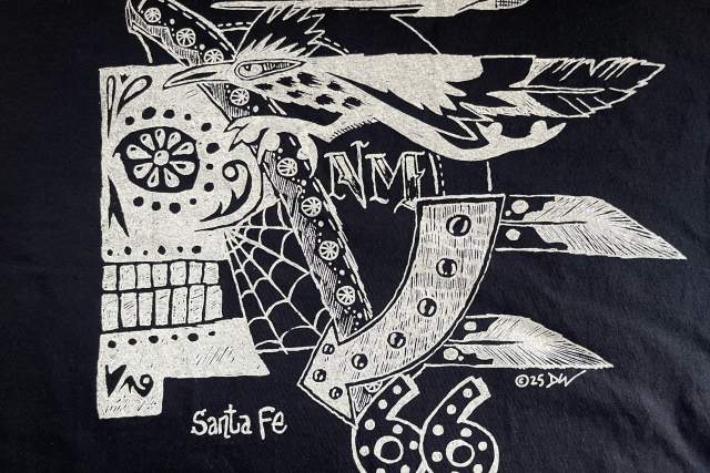 Graphic T-shirt design featuring a stylized skull with a bird above it and the text "Route 66" and "Santa Fe." The design includes artistic elements like floral patterns and geometric shapes.