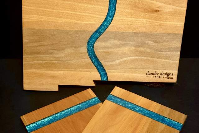 A set of wooden coasters and a matching board with a blue resin river design, branded by Dandee Designs.