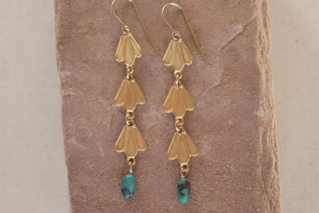 Gold raindrop shaped earrings with turquoise accents displayed on a stone slab.