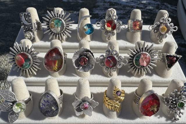 A display of various rings featuring colorful gemstones, set on white stands against a sunlit background.