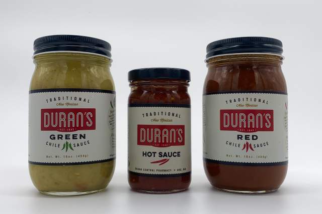 Three jars of Duran's Chile Sauce lined up, from left to right: Duran's Green Chile Sauce, Duran’s Hot Sauce, and Duran's Red Chile Sauce. Each is labeled traditionally with clear text against a bright background.