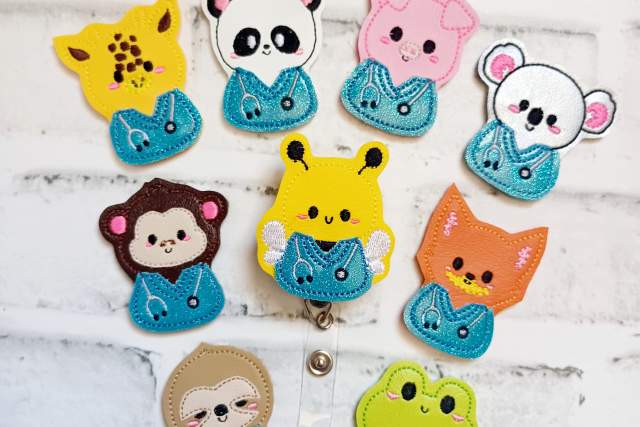 Colorful felt keychains featuring various animal designs, including a panda, pigs, a koala, monkeys, bears, and foxes, arranged on a white brick background.