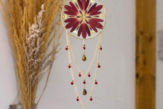A decorative hanging ornament featuring a circular disk with a red and white floral design, adorned with chains of red beads and golden accents, displayed against a neutral wall background.
