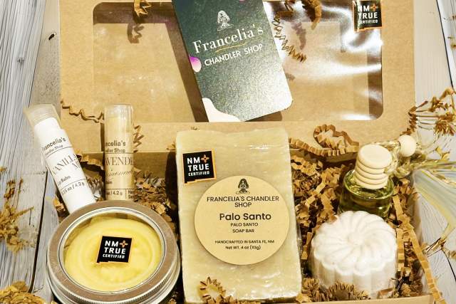 An elegant gift box labeled "Francella's Chandler Shop" containing various bath items including a candle, soap bar, body lotion, and other accessories, arranged on a wooden surface with decorative leaves.