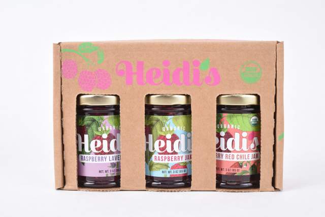A display box of Heidi's organic jam, featuring three jars labeled Raspberry Lavender, Raspberry Jam, and Raspberry Red Chile Jam, against a white background.